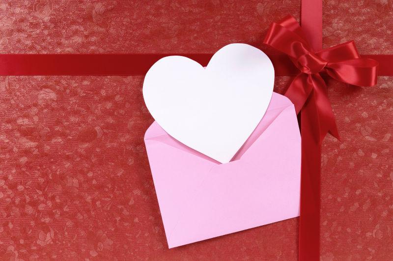 红色的有丝带的背景上粉色信封里的白色心形卡片