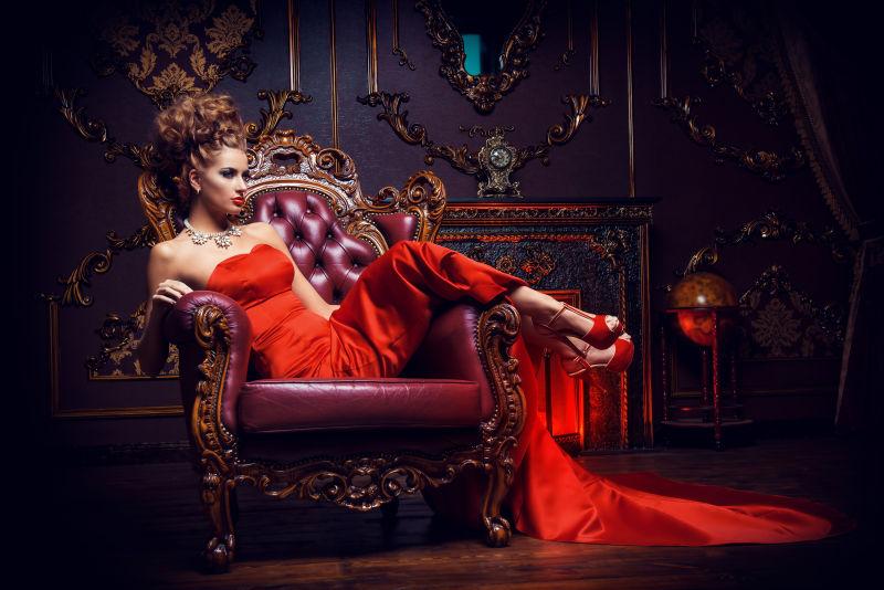 复古风格背景下穿着红色长礼服半躺在红色沙发上的美女
