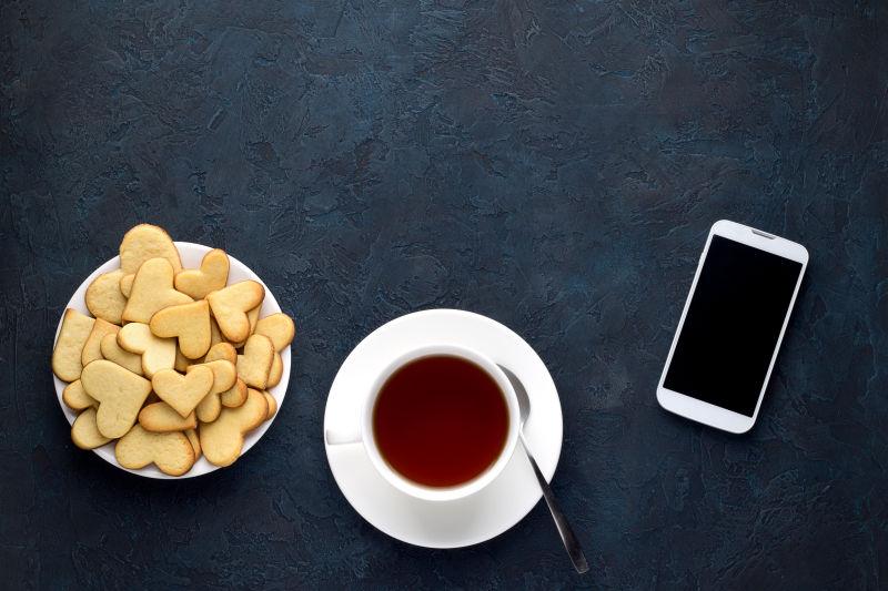 一杯茶和心形饼干和石头上的智能手机