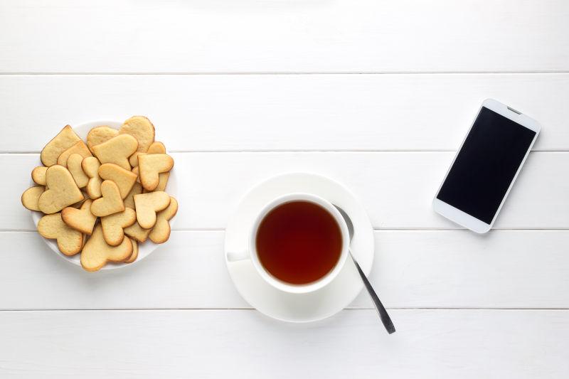 早餐茶和心形饼干和智能手机在木桌上