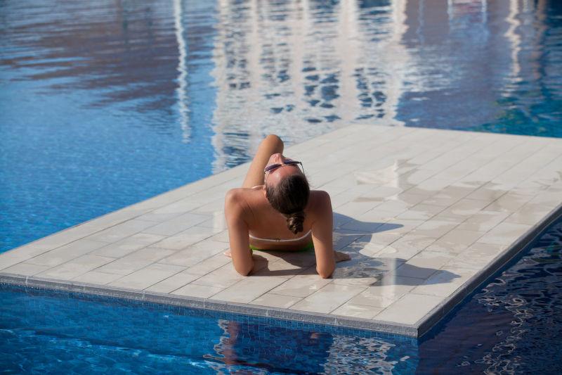 游泳池附近的性感女子享受日光浴