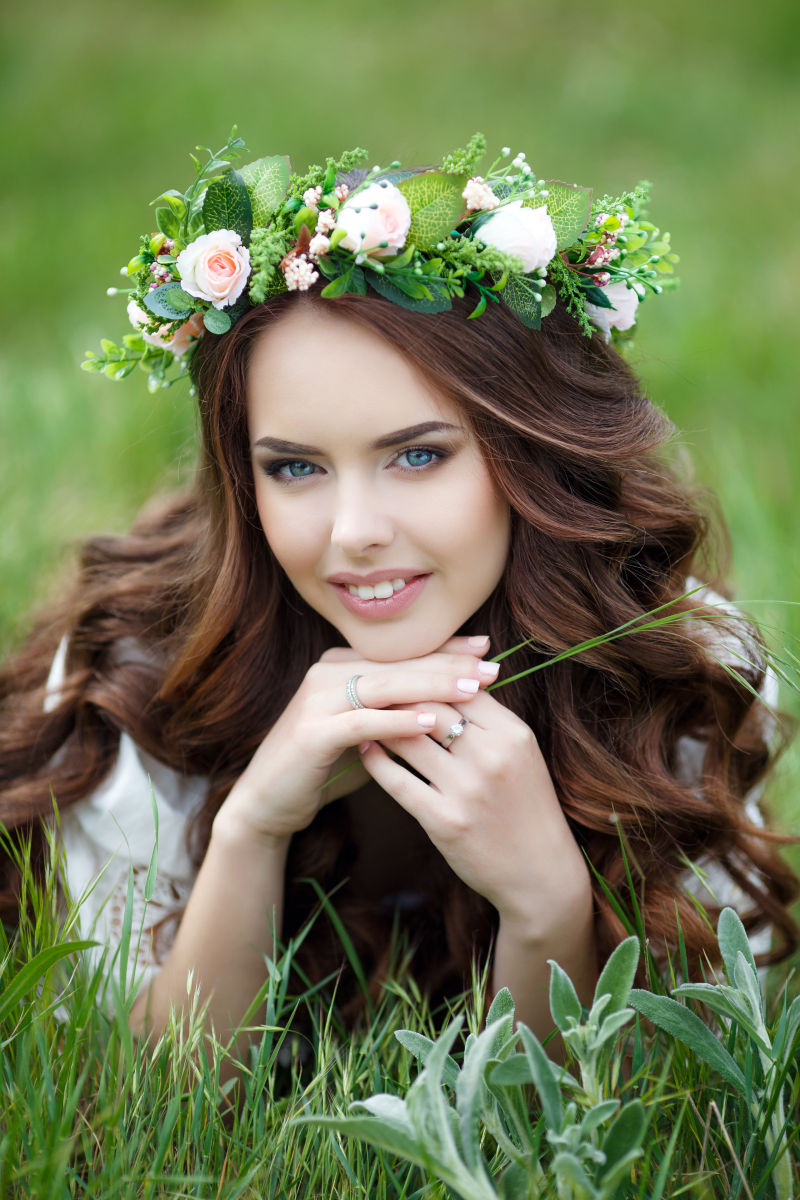 年轻长卷发美女戴着花环蹲在草丛里