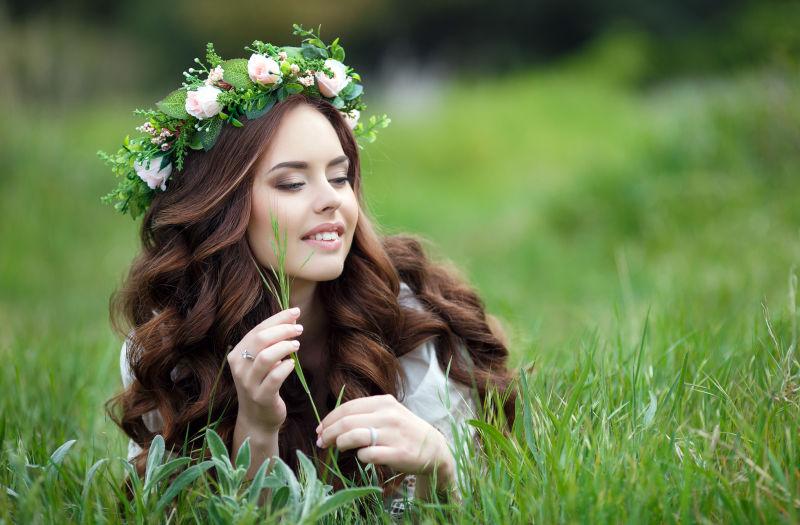 蹲在草丛里微笑的年轻美女戴着花环