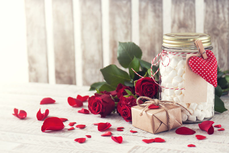 木制背景上带棉花糖的罐子礼物和玫瑰花束