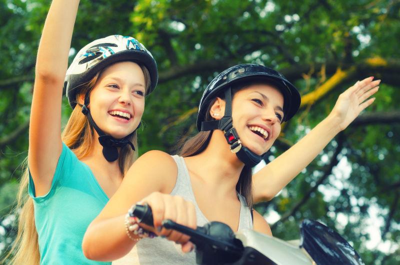 两个微笑的少女女友骑滑板车