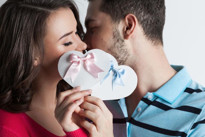 白色背景中拿着纸质心形卡片接吻的情侣