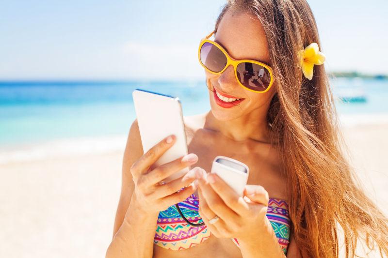 女性旅游者使用便携式电源银行在海滩上充电