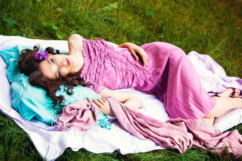 美丽浪漫的年轻女子穿着粉红色连衣裙躺在枕头上的夏日花园