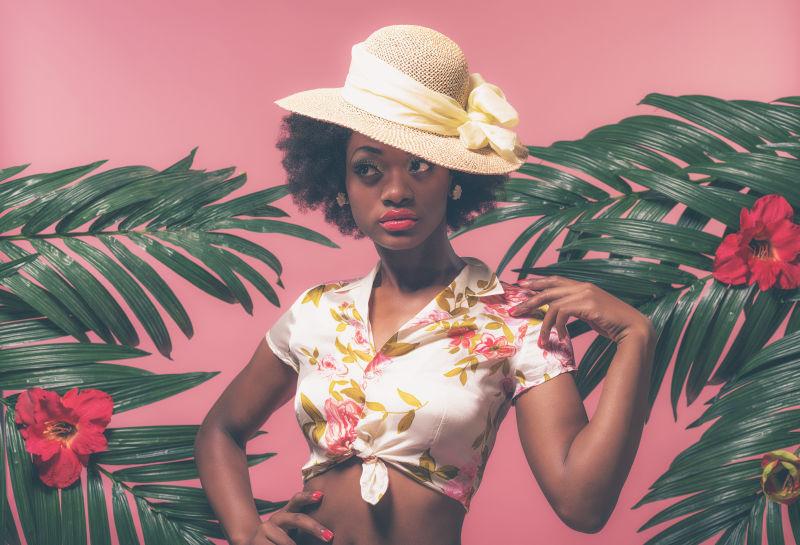 粉红色背景下用棕榈叶夹帽子的性感的非洲裔美国人