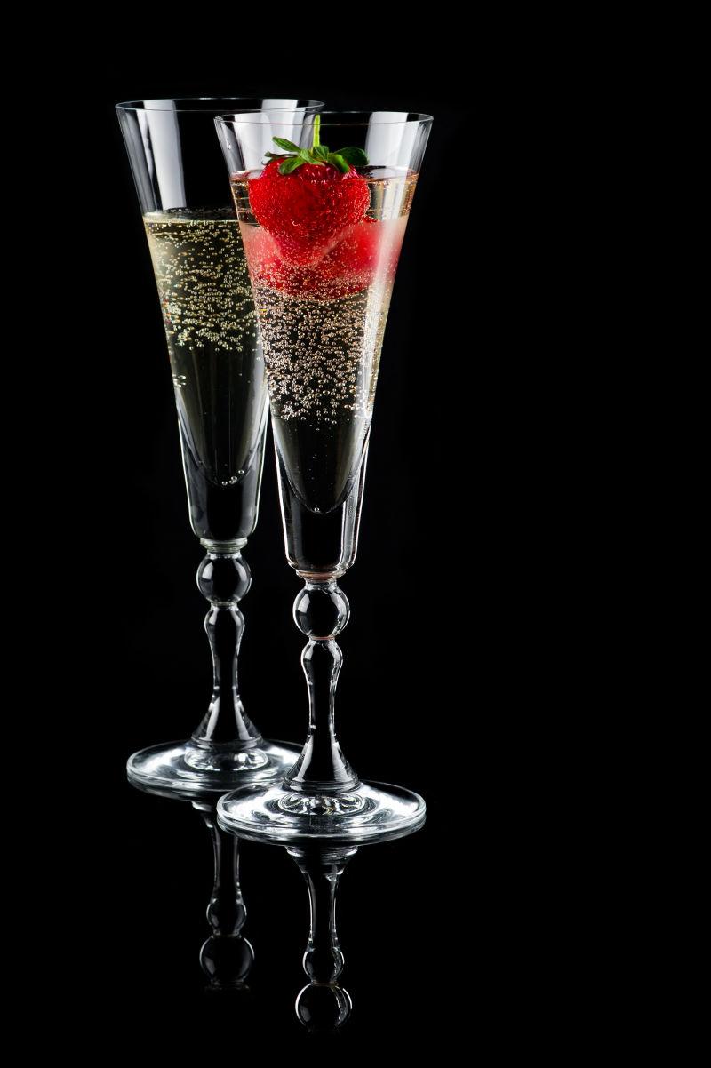 黑色背景上的两杯起泡葡萄酒（香槟）和草莓