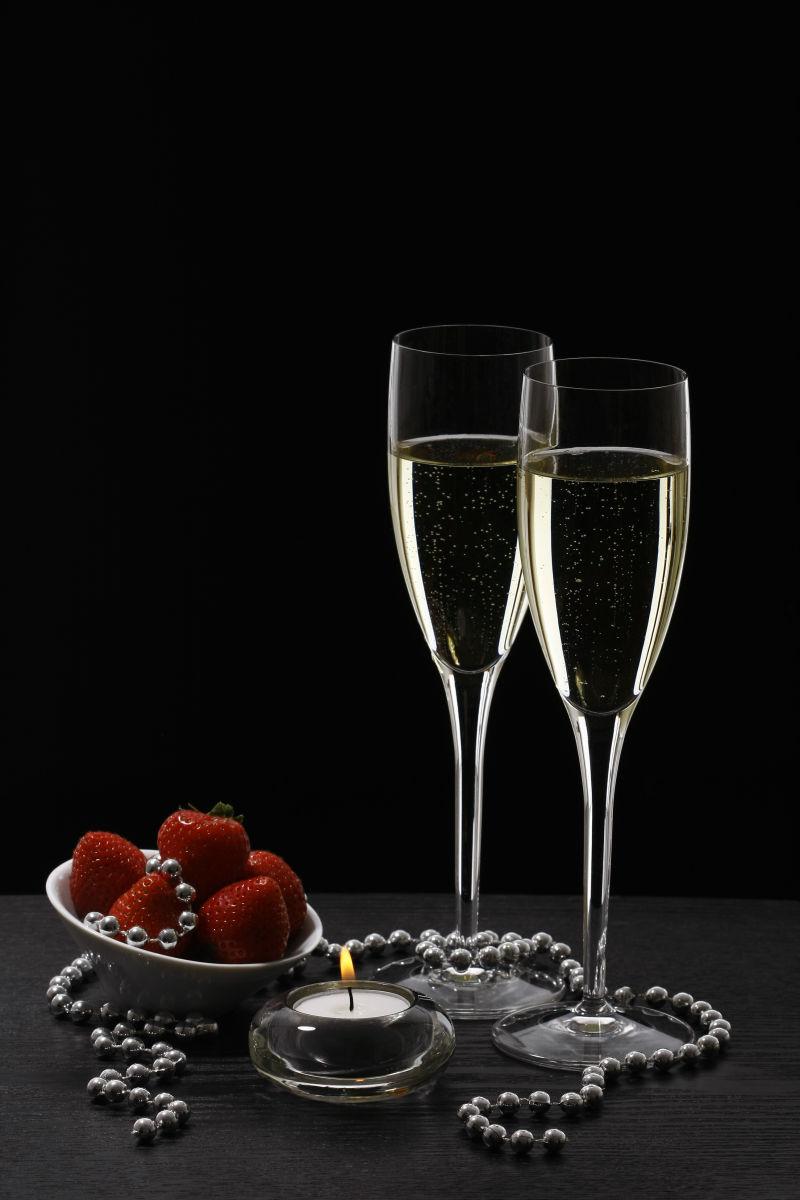 黑色背景上的珍珠项链和草莓与香槟酒