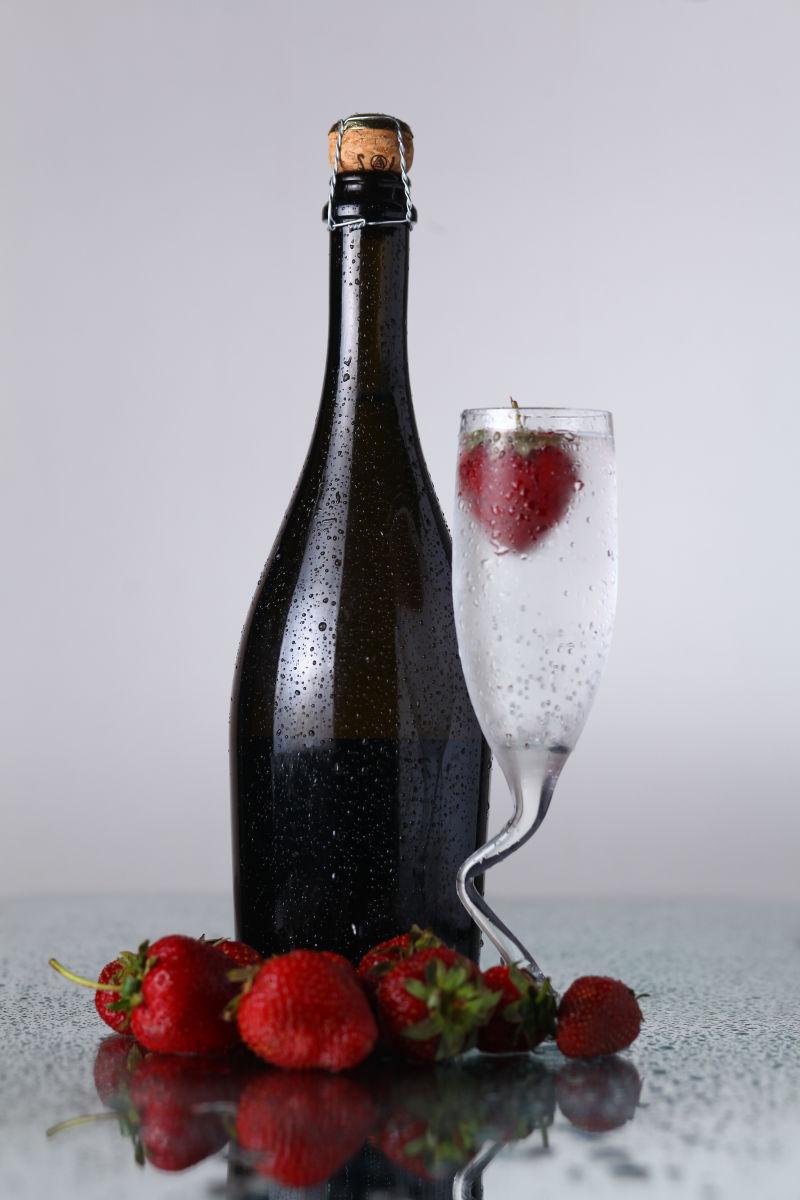 灰白色背景上的冰镇香槟瓶和草莓装饰的高脚杯