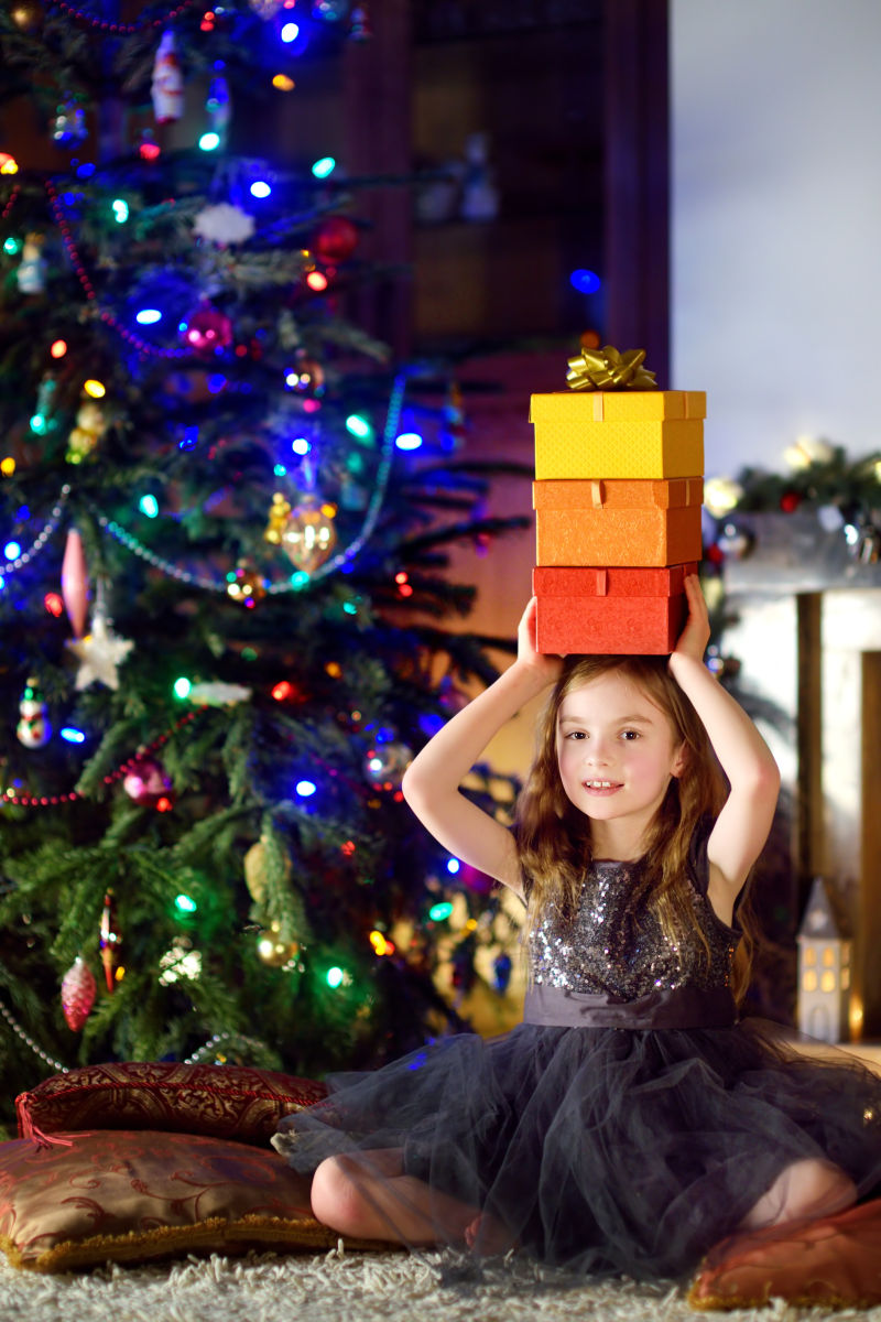 圣诞树边顶着礼物盒的小女孩