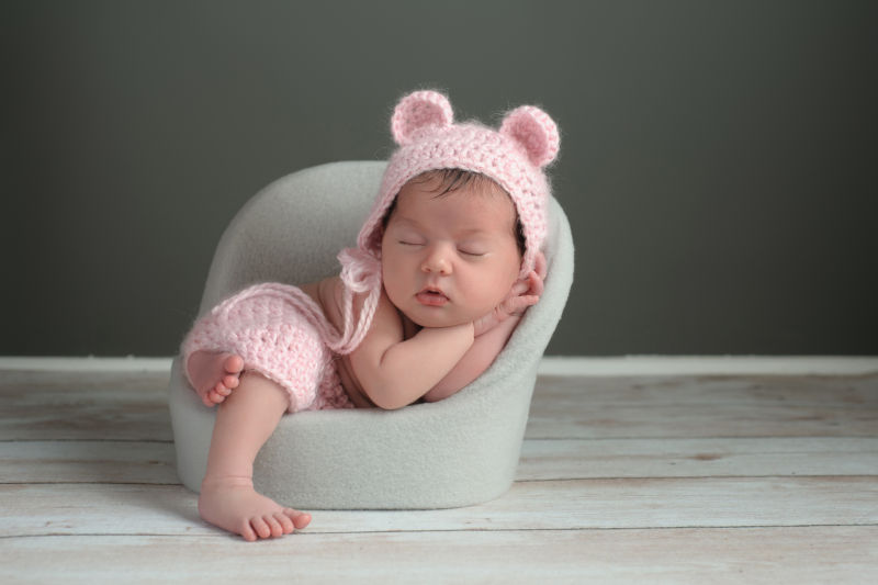 戴着粉红色帽子靠在灰色沙发上睡觉的婴儿
