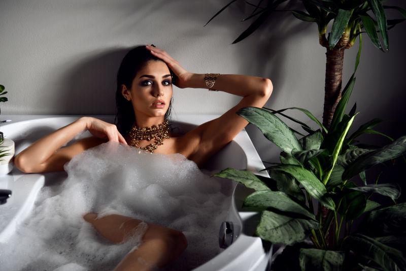 灰色背景下植物旁躺在浴缸泡沫里的性感美女