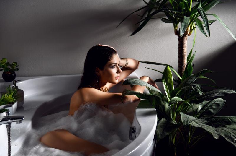 灰色和植物背景下的浴缸泡沫里的性感美女