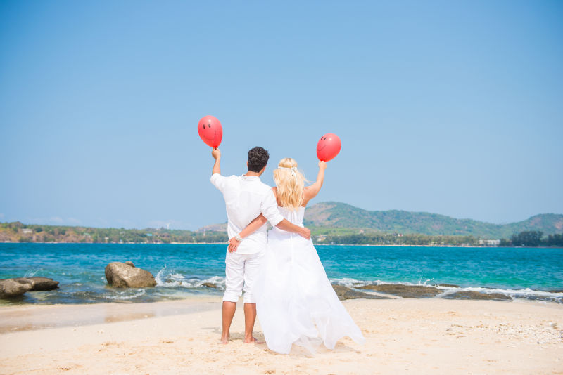 新娘和新郎在海滩上抱着红色气球