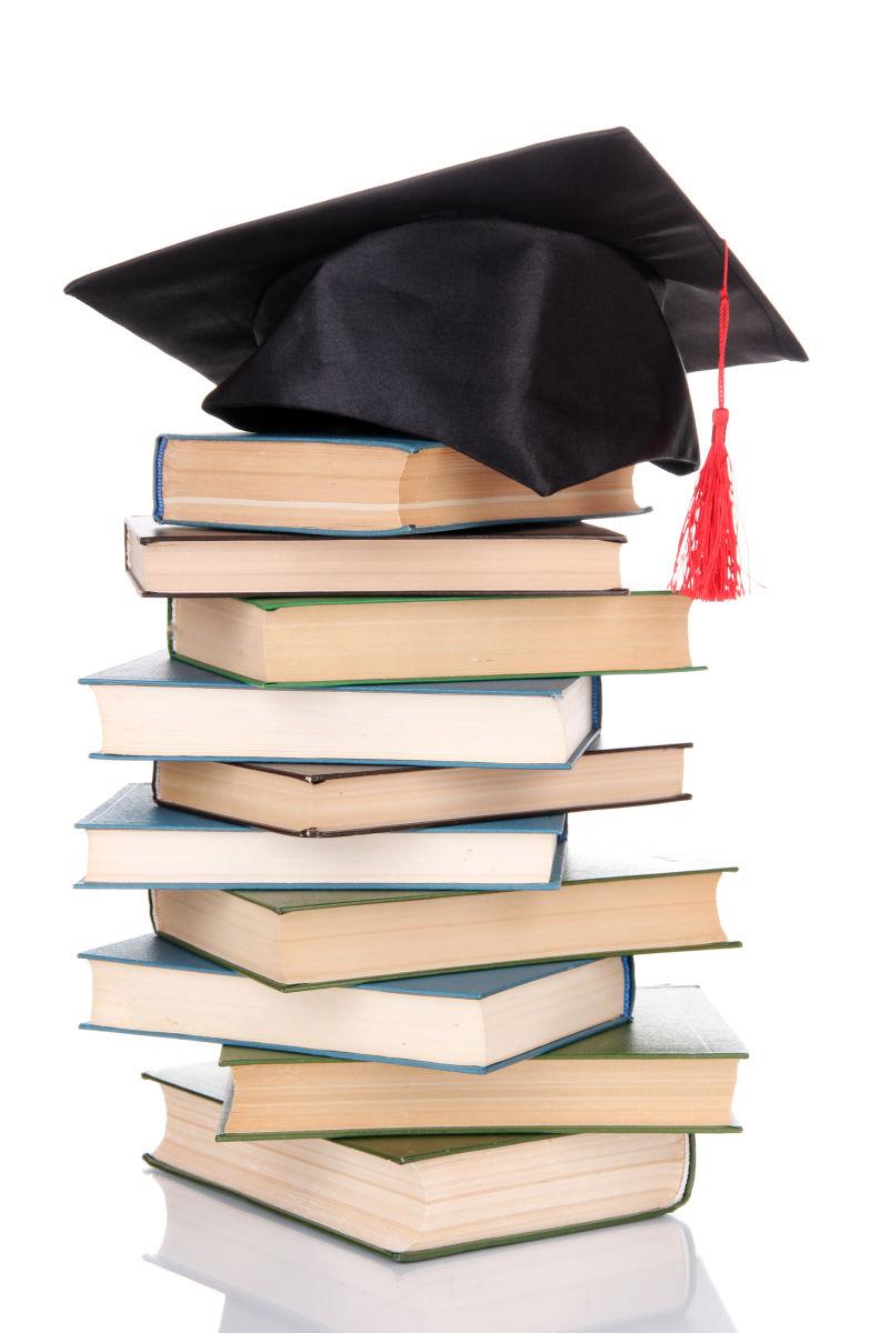白色背景中的一堆书和毕业帽