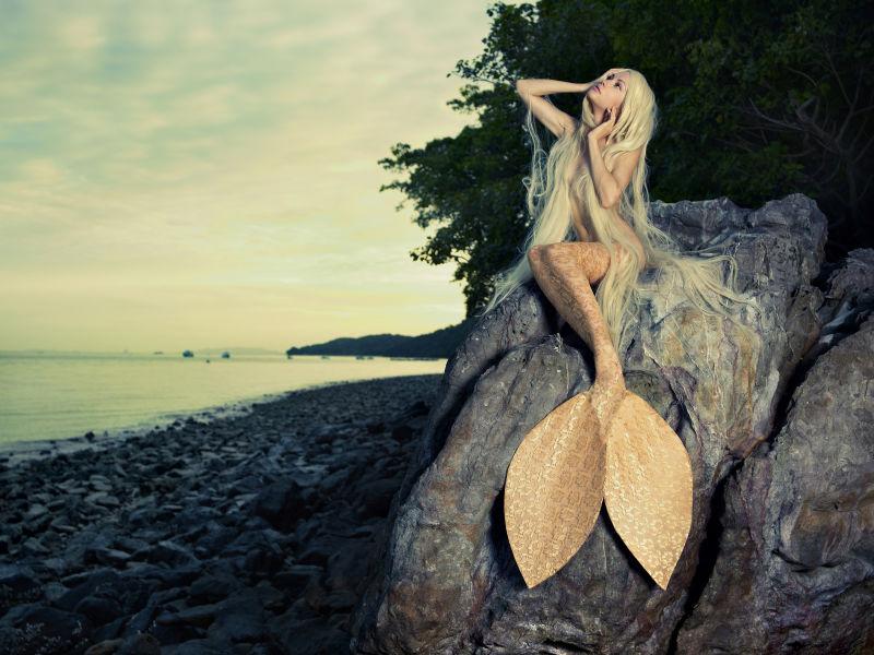 美丽的美人鱼坐在海边的岩石上