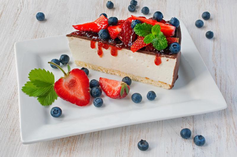 新鲜草莓和蓝莓芝士蛋糕在木桌上白色盘里