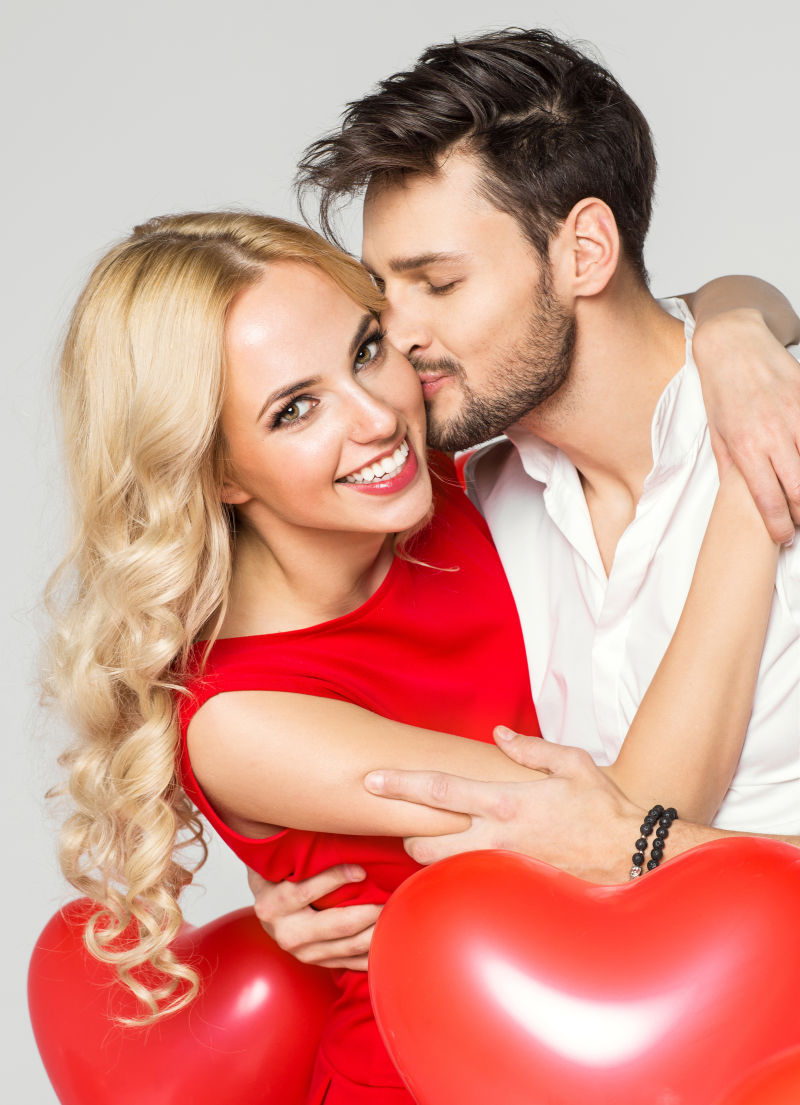 拥吻的情侣拿着情人节的浪漫红色气球