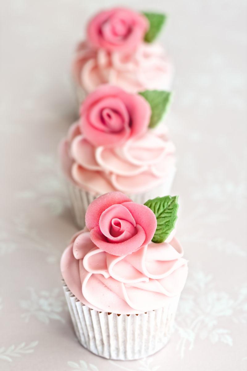 粉色桌上三个美味的玫瑰花蛋糕
