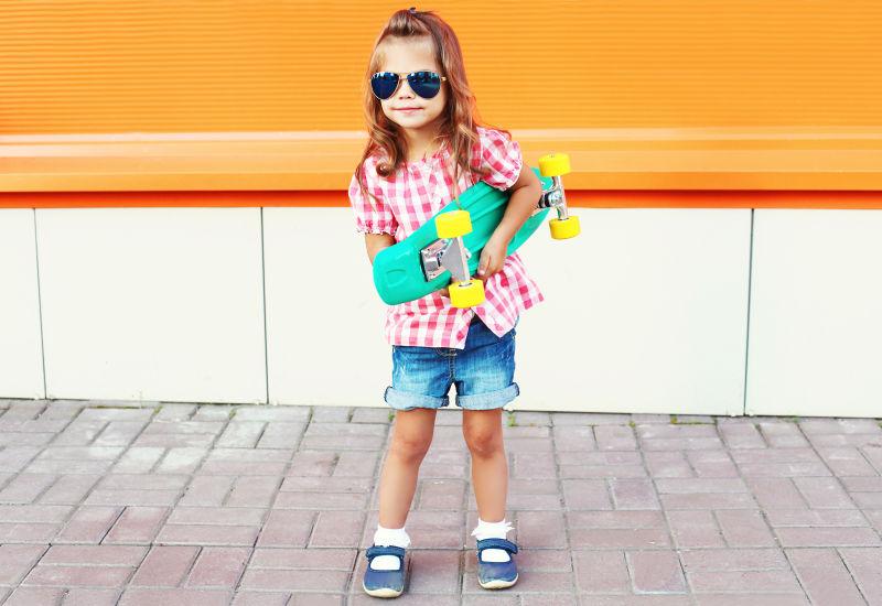 城市街头带着太阳镜抱着滑板的小女孩