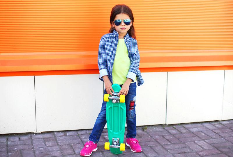 城市街头带着太阳镜拿着滑板耍酷的小女孩