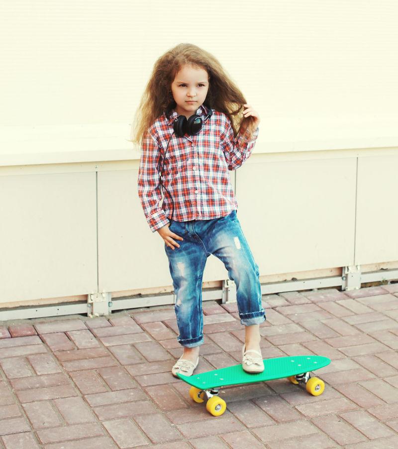 户外背景中玩滑板的时尚小女孩