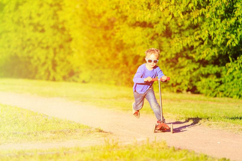 小男孩在夏日公园骑滑板车