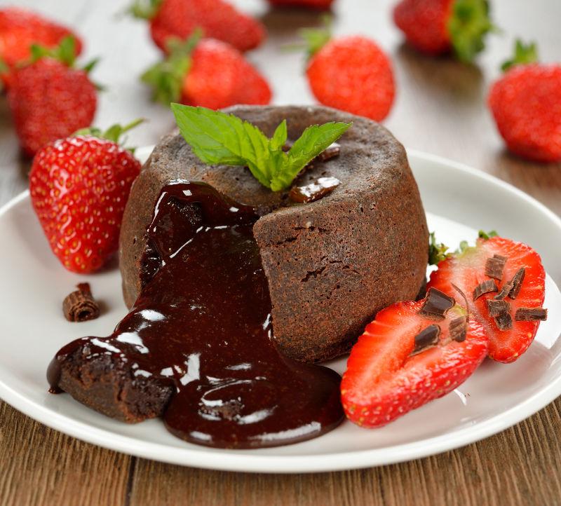 木桌上白色盘子里的巧克力和草莓蛋糕