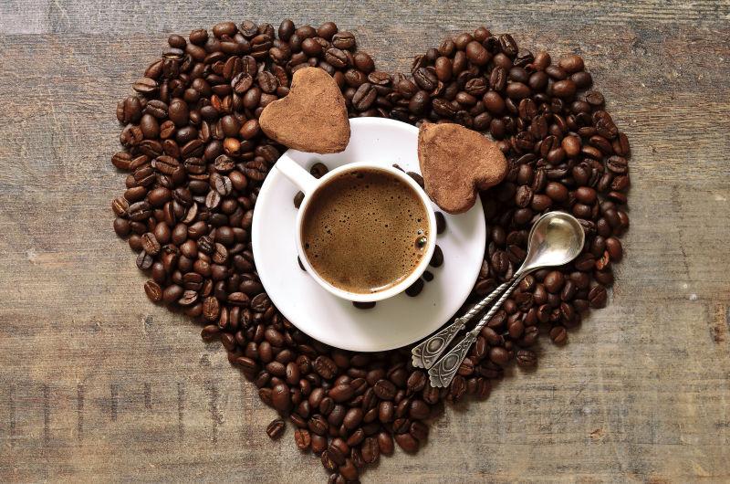 木桌上摆成心形的咖啡豆上的一杯咖啡和两块心形巧克力饼干