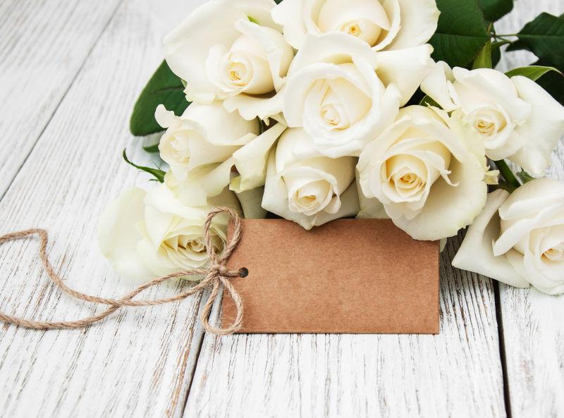 白木桌上的白玫瑰和空白标签