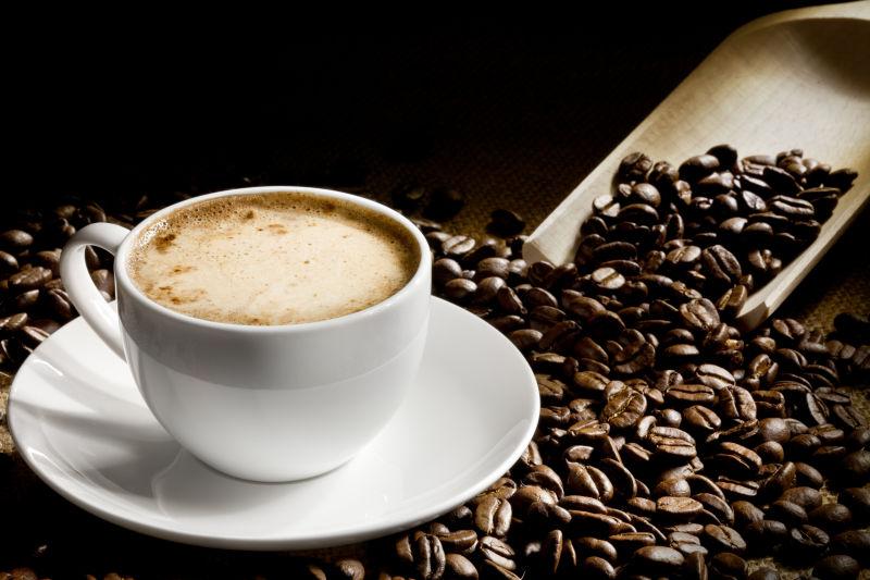 黑色背景下的美味的一杯咖啡和棕色咖啡豆