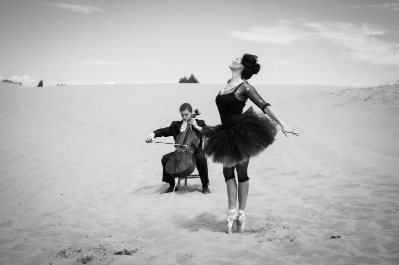 独奏大提琴家为一位优雅的芭蕾舞演员在荒芜的沙漠中跳舞而演奏