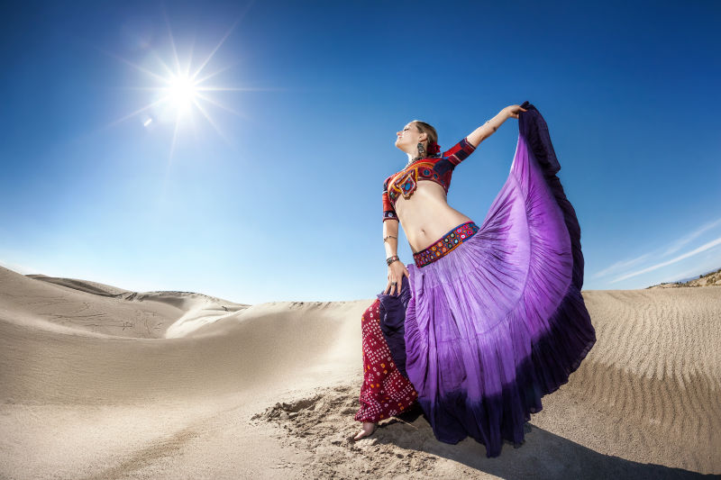 紫色裙子里的女人在蓝天的沙漠里跳舞