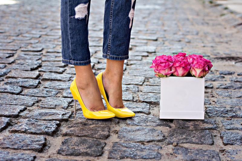 粉红色的玫瑰和女性的腿在牛仔裤和高跟鞋的黄色鞋