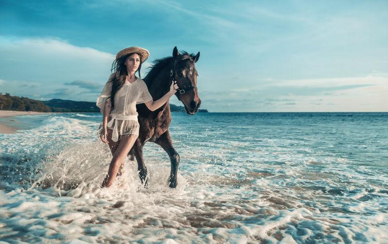 性感的黑发女人海滩水里牵着马