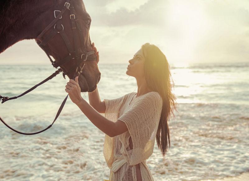 迷人的女士在海边抚摸她心爱的马