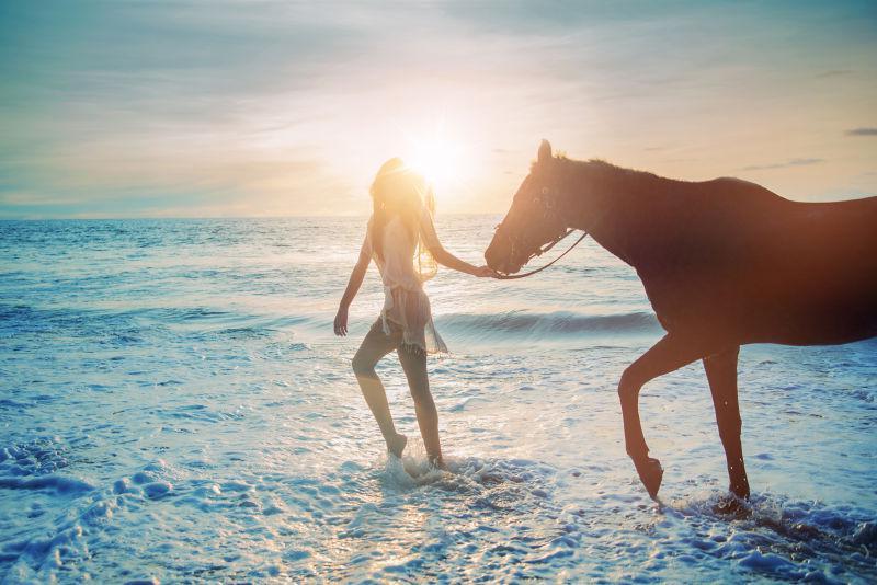漂亮的女士带着她的宠物马在海滩散步