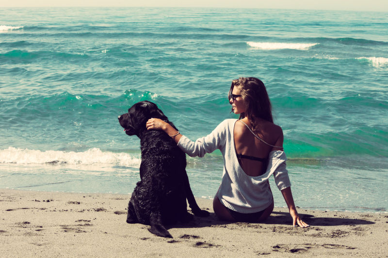 年轻的女人和她的狗坐在沙滩上