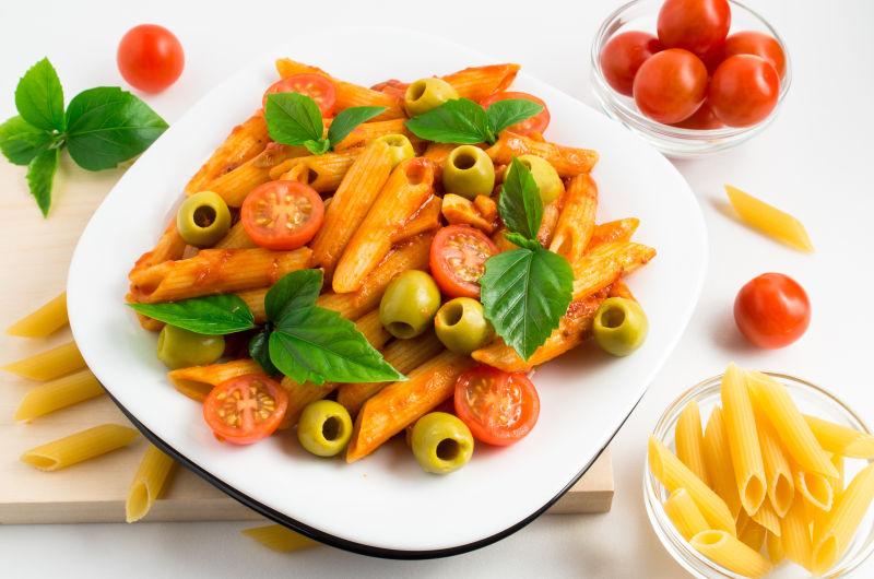 一种用樱桃番茄橄榄和香草装饰在木托盘上的意大利面食白盘子
