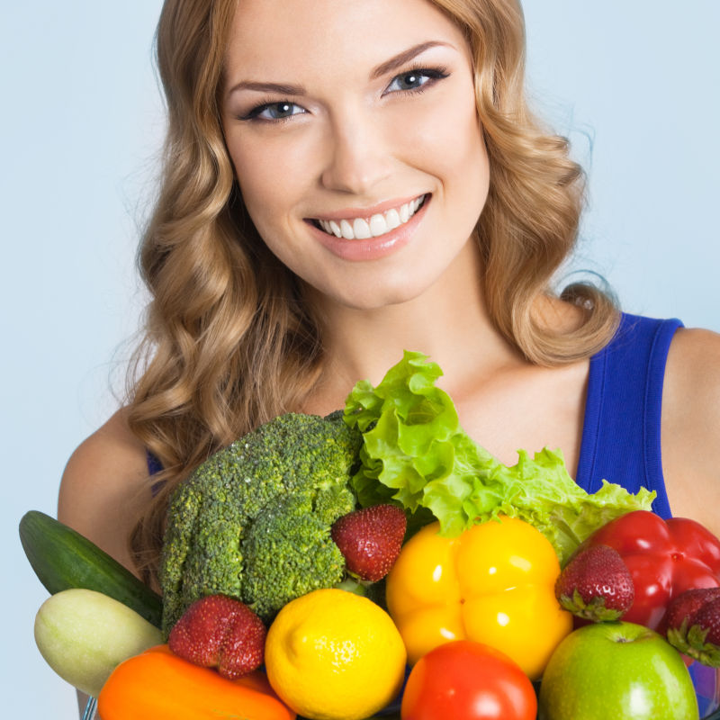 蓝色背景中的快乐美丽的女人与健康素食
