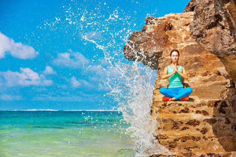 坐在海滩岩石上练习瑜伽的女人