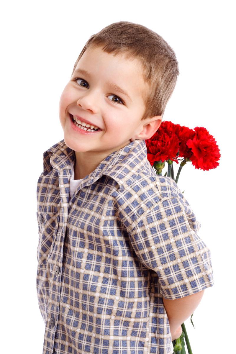 白色背景下微笑的男孩藏着一束红色康乃馨
