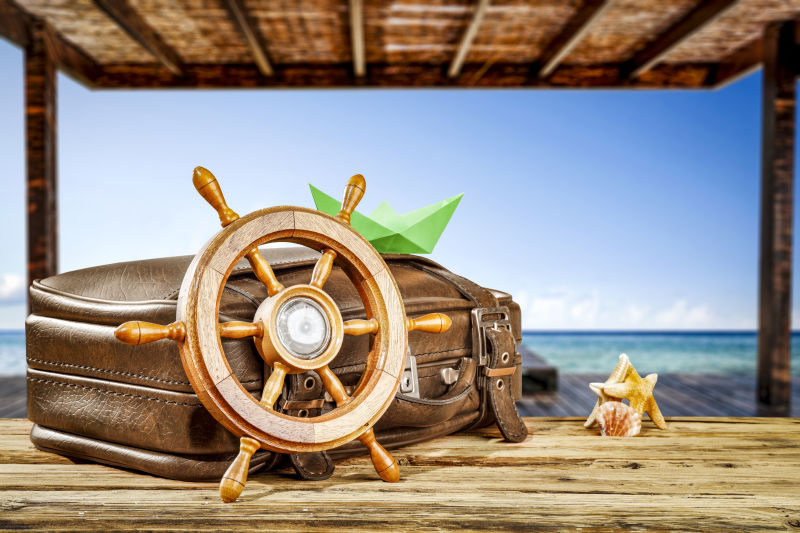木制背景上的旅行箱和船舵