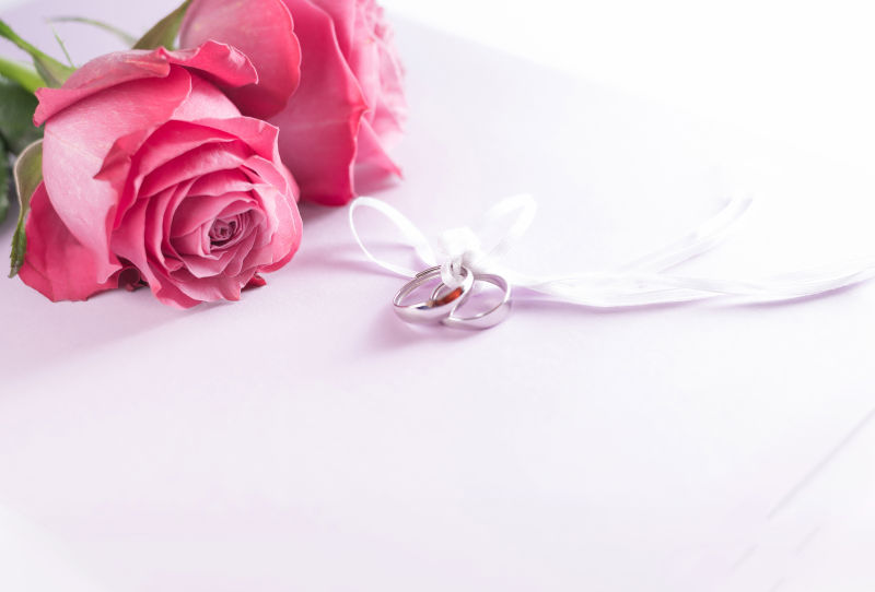 玫瑰花前一对系在一起的结婚戒指