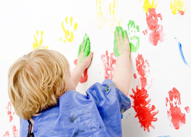 可爱的孩子用沾满颜料的手在墙上作画