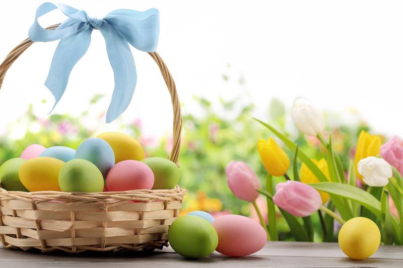 白色背景下褐色桌上篮子里的复活节彩蛋和郁金香花朵