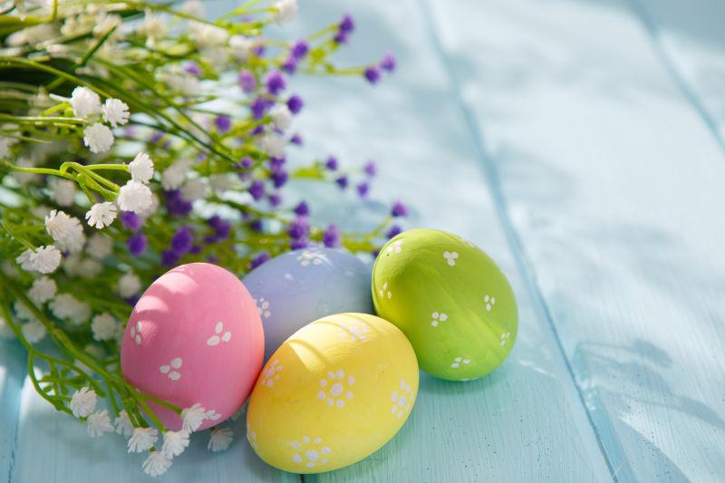 淡蓝色木纹理桌上的复活节彩蛋和紫色的满天星花朵